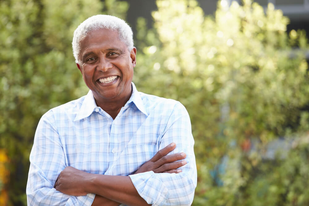 Senior man with gray hair and arms crossed smiling at camera